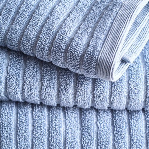 A neat stack of folded pale blue, eco-friendly Canningvale Alessia Cotton Bamboo Rib Hand Towels in Fresco Blue on a gray background.