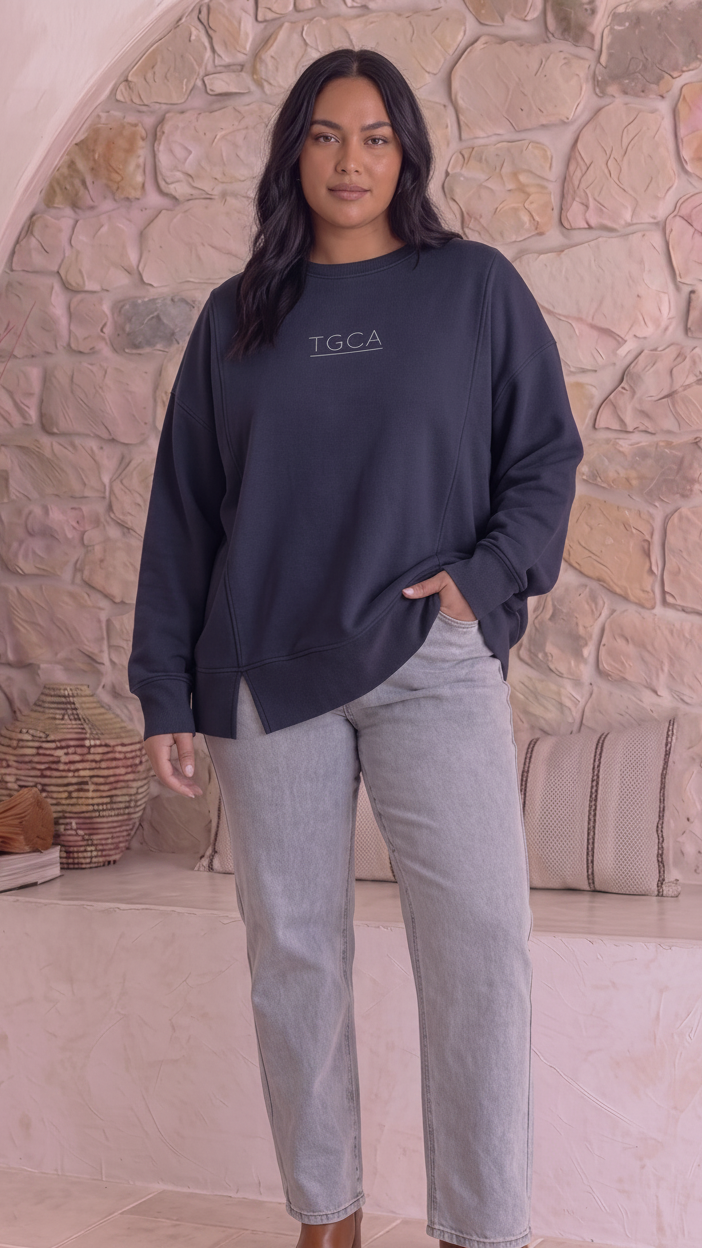 A woman stands in front of a stone wall wearing a dark navy long-sleeve sweatshirt with &