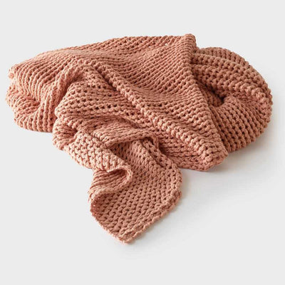A soft, coral-colored Abrazo Throw - Rose Dust by Eadie Lifestyle casually folded on a light background.